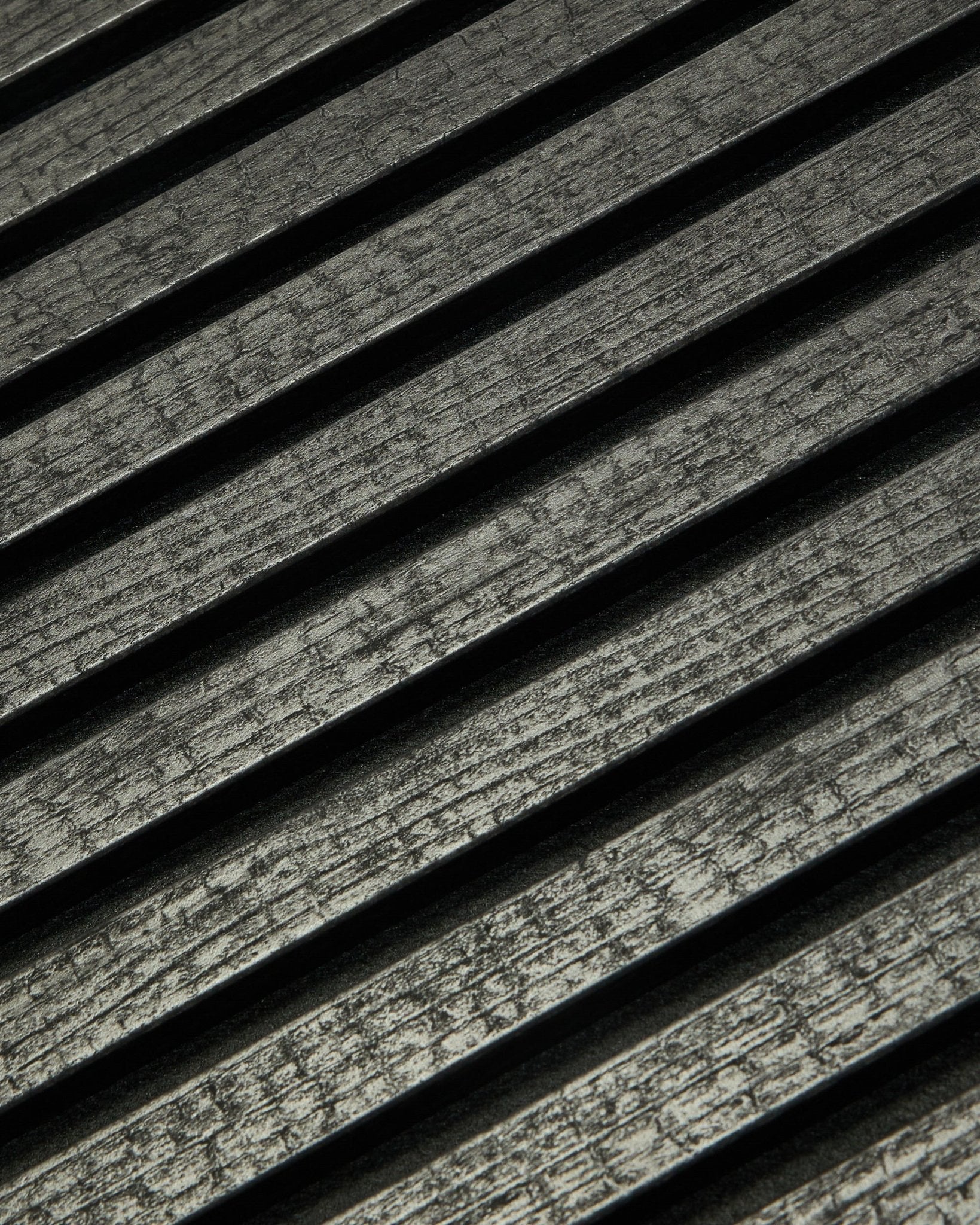 Close-up van WoodUpp Rebel Akupanel in Charcoal (240x60 cm), met black, gegroefde akoestische latten die diagonaal zijn geplaatst voor betere geluidsabsorptie.